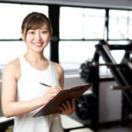 Asian female trainer standing with a smile in the training gym